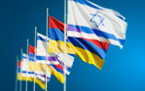 Vibrant national flags of Israel and Armenia waving against a clear blue sky.
